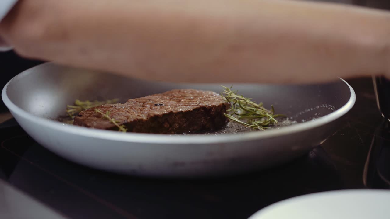 Close up of chef putting steak on a frying pan with some rosemary and leaves