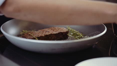 close up of chef putting steak on a frying pan with some rosemary and leaves