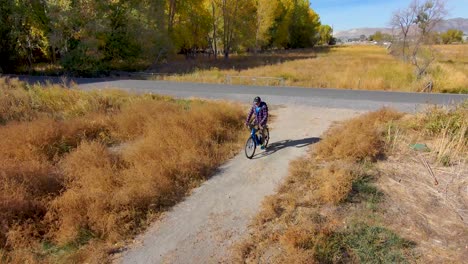 Senior-bicycles-off-a-paved-trail-onto-a-gravel-trail-and-gets-off-his-bicycle---aerial-view