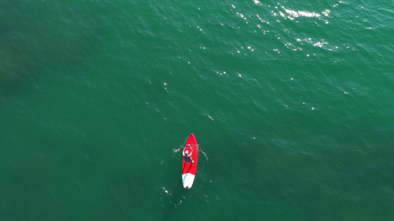 Lifeguard paddling on red paddle board in turquoise water