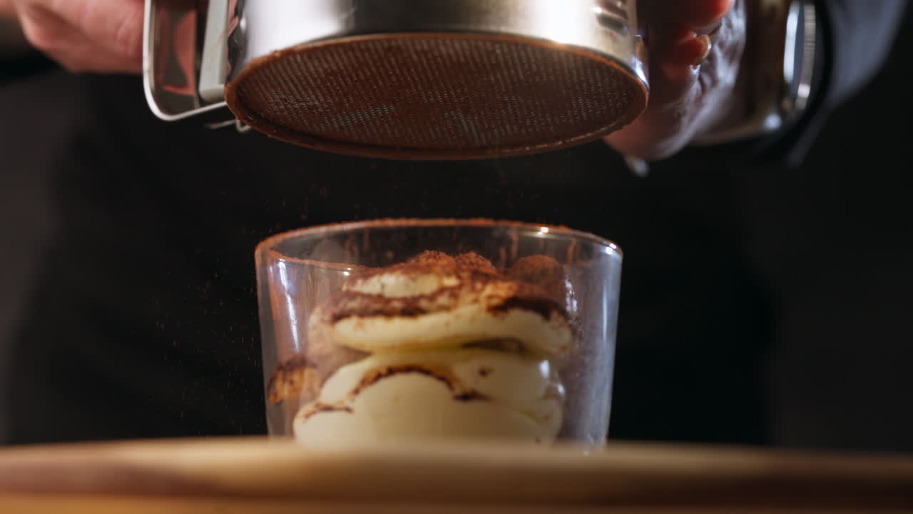 Chef che aggiunge cacao in polvere a un dessert tiramisù. Primo piano al rallentatore.