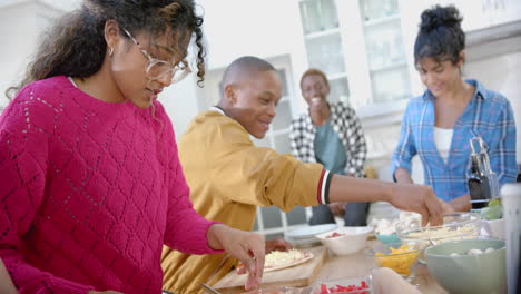 Happy-diverse-group-of-teenage-friends-cooking-and-making-pizza-in-kitchen,-slow-motion