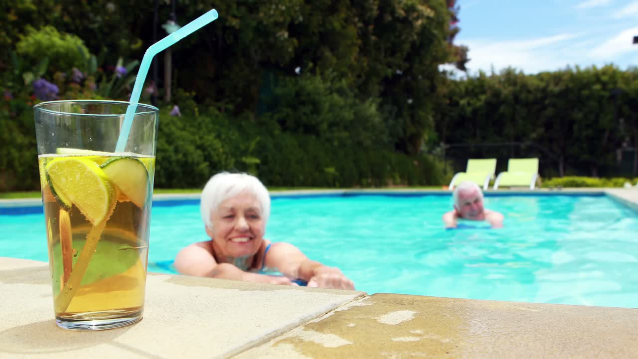 Senior woman having glass of iced tea in pool
