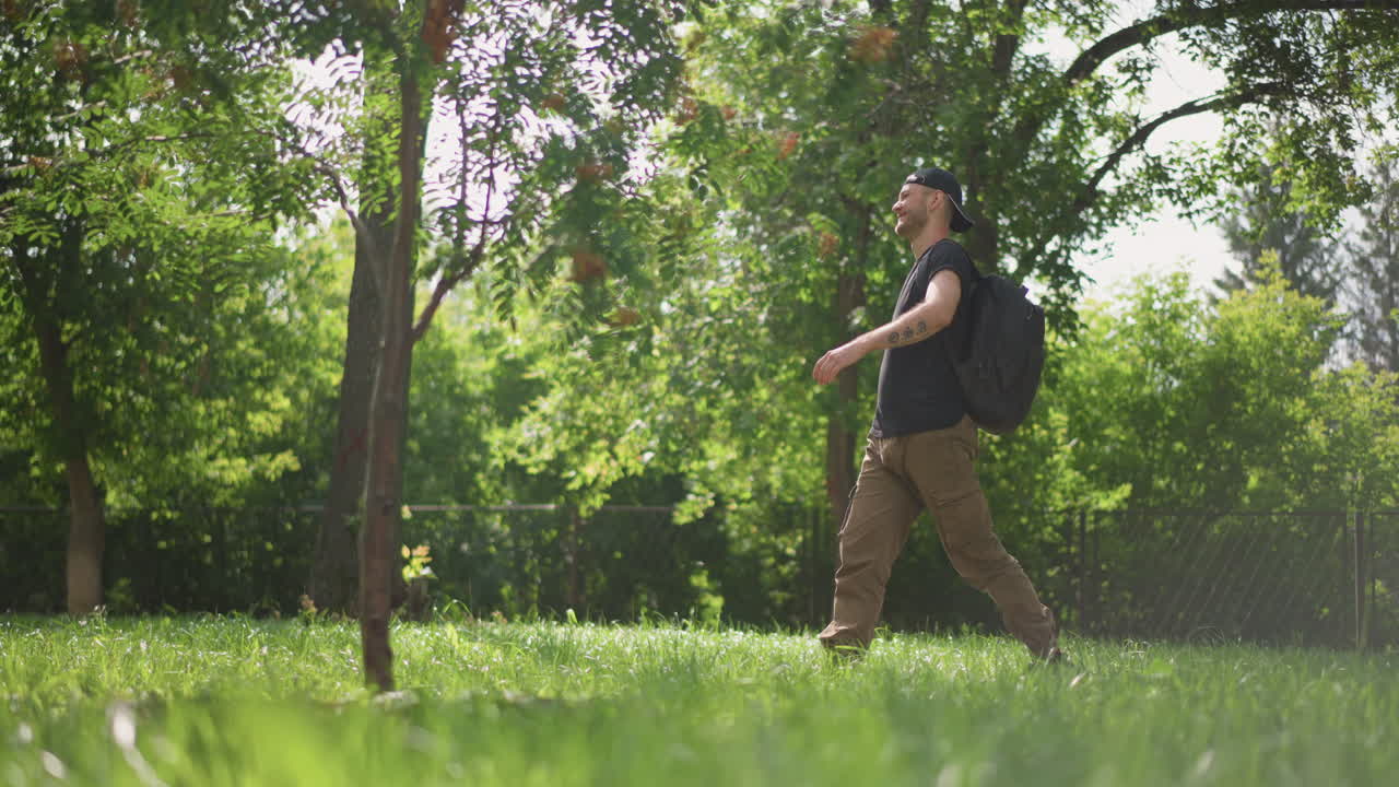 Gentle Walk Beneath Towering Trees, Solitary Figure Ambles Slowly Across Sundrenched Grassy Landscape, Lone Man With Backpack Moves At Leisurely Pace Under Shade Of Majestic Tall Trees