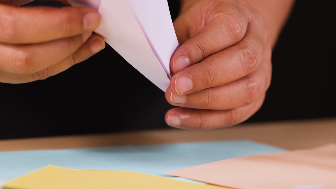 Close-up shot of hands carefully folding white paper into an origami airplane on a table