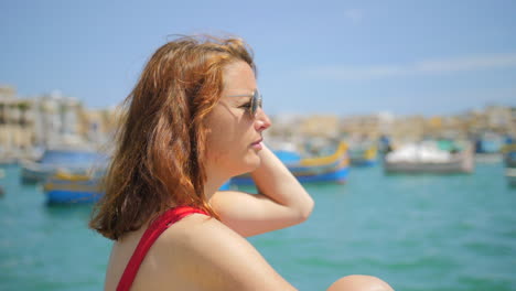 chica pelirroja de perfil admirando la belleza del pueblo pesquero de marsaxlokk en malta