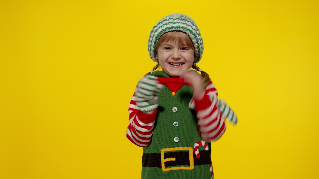 Dívka v kostýmu vánočního skřítka, pomocníka Santy, mává na pozdrav rukou. Ahoj, nazdar, gesto pozdravu.