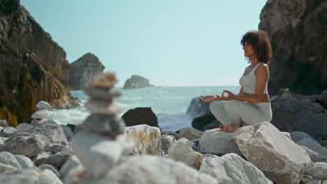 woman meditating lotus pose on stone ursa beach vertically. girl practicing yoga