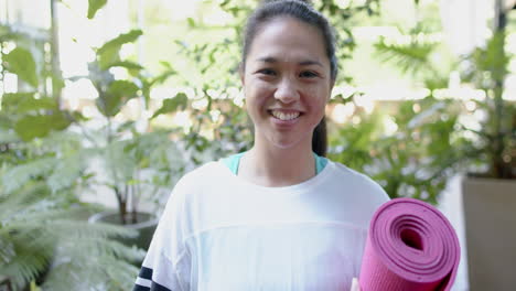 Glückliche-Asiatische-Frau-Mit-Trainingsmatte-Lächelt-Auf-Sonniger-Terrasse,-Zeitlupe