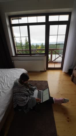 woman working from home with a laptop in a cozy bedroom with a mountain view