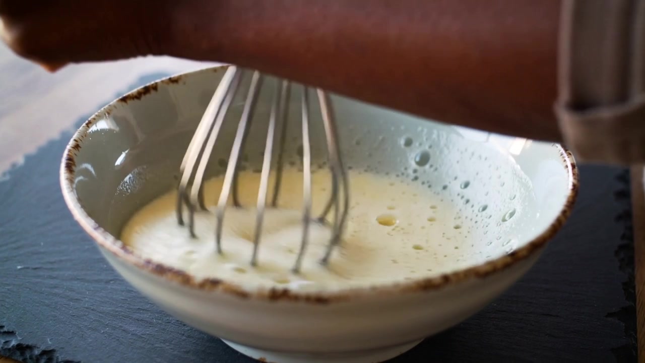 Vispilä kulhossa saa kokin, hiha käärittynä, vispaamaan keltaista seosta kotipöydällä kuohkeaksi.