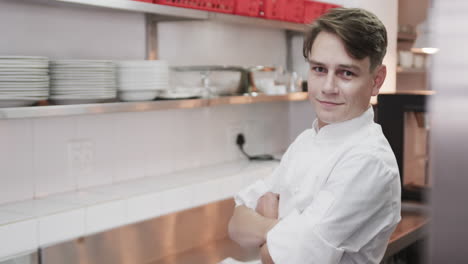 portrait of caucasian male chef with crossed arms and smiling in kitchen, copy space, slow motion