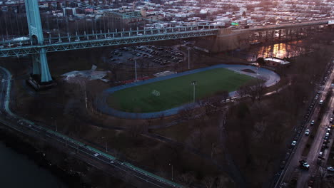 aerial view tilting away from the astoria park running track revealing traffic on the robert f. kennedy bridge, sunset in new york, usa