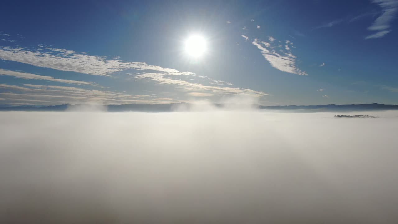 Aerial flight by drone over a foggy landscape on a beautiful blue sky sunny day with mottled clouds