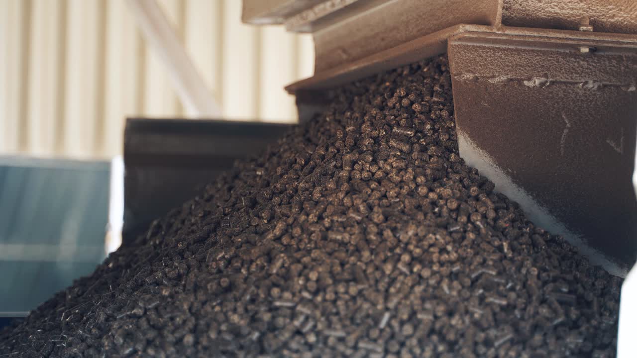 Production of fuel briquettes. Pile of brown pellets pouring out from industrial machine. Close-up
