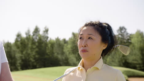 Asian-woman-talking-to-her-husband-with-golf-club-on-her-shoulder