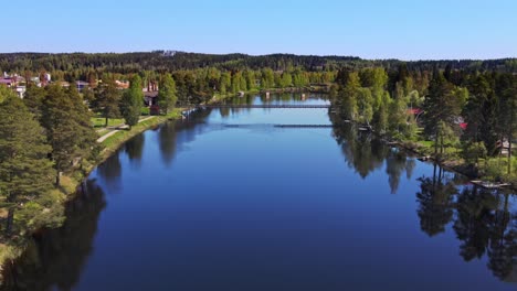 vasterdalaven river and the town of vansbro under clear blue sky in dalarna county, sweden. ascending drone shot