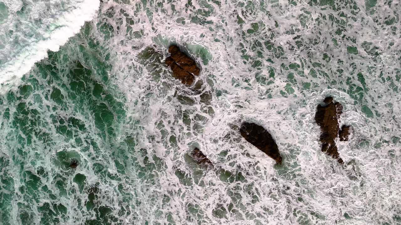 Pull in, aerial, birds eye view, drone shot of large, strong waves, powerfully crashing on a set of secluded rocks