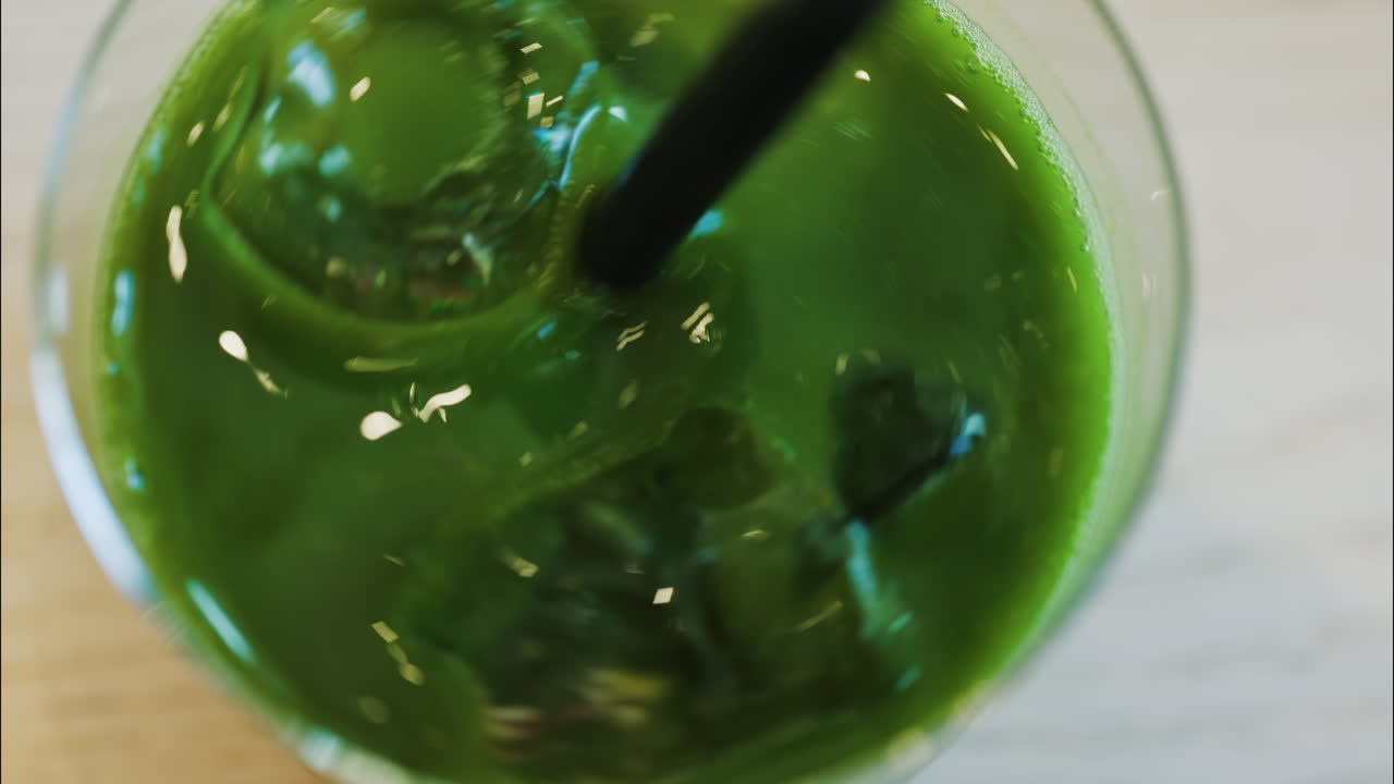 Close up of a hand mixing an iced matcha in a glass with a black straw at a cafe