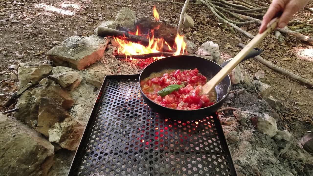 Cooking the italian delicious tomato and meat sause, sugo, in the woods on the wildfire