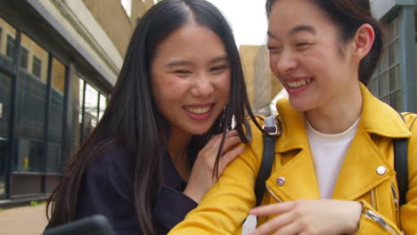 two smiling young female friends posing for selfie in urban setting together 1