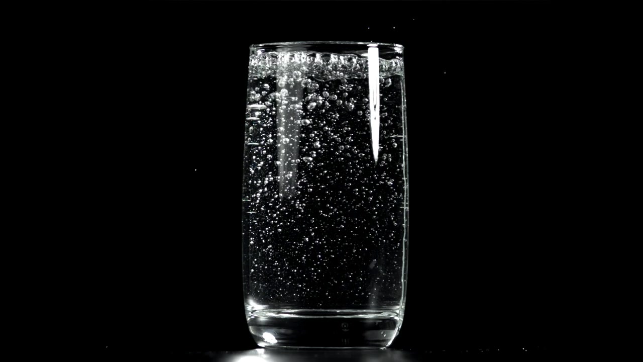 Bollicine che salgono in un bicchiere di acqua frizzante su sfondo nero