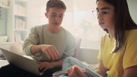 two caucasian teenagers sitting on floor and learning from books and laptop