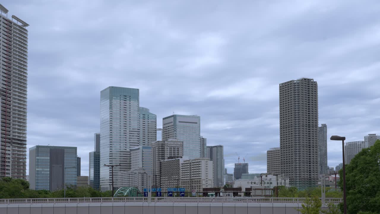 A wide shot of the Tokyo skyline with modern skyscrapers against a dramatic, cloudy sky