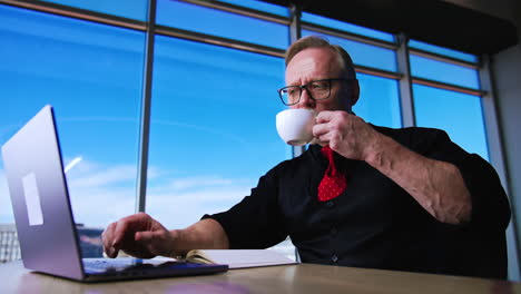 Caucasian businessman working on laptop and drinking coffee. Low angle view on the man having coffee break at workplace.