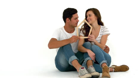 smiling couple sitting on the floor holding house shape