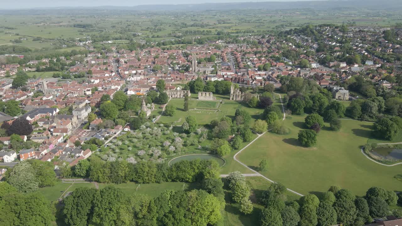 Aerial view of the Glastonbury Abbey ruins an 8th century monastery and gardens. Drone rotating to the riight showing the the extension of the Glastonbury abbey and Glastonbury town. 4K, 60fps.