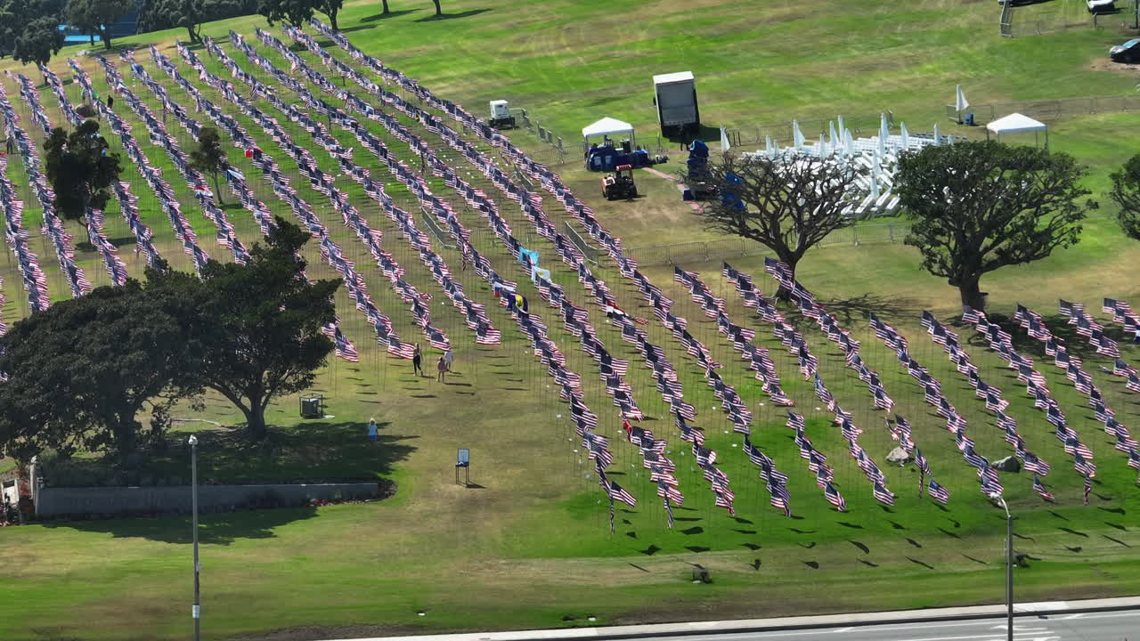 Telephoto drone shot circling many US flags on a lawn, next to a road in LA