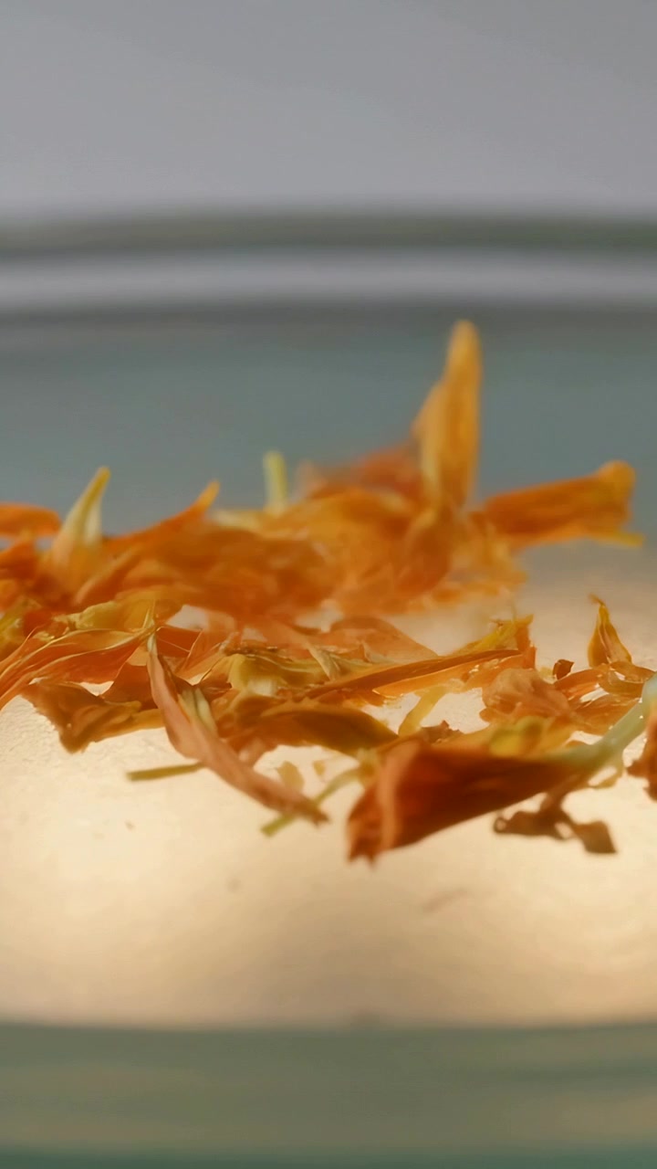 Vertical video: Puff causing orange petals lifting and fluttering in glass bowl on table