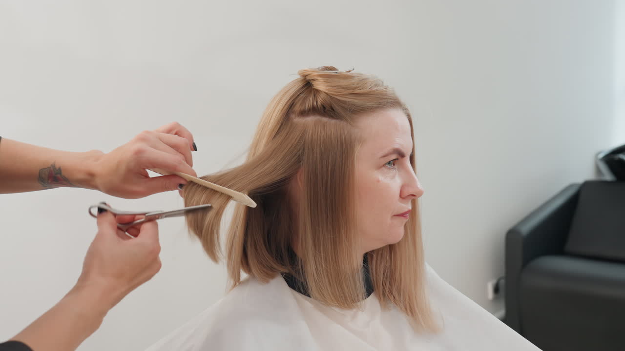 blonde woman seated in salon, stylist sections hair and trims precise bob with comb and scissors, white minimalist interior, cape draped, calm focused atmosphere, professional grooming and subtle