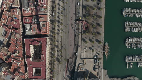 Birds-eye-shot-of-vehicles-driving-on-road-along-marina.-Sunny-day-at-sea-coast-in-city.-Barcelona,-Spain