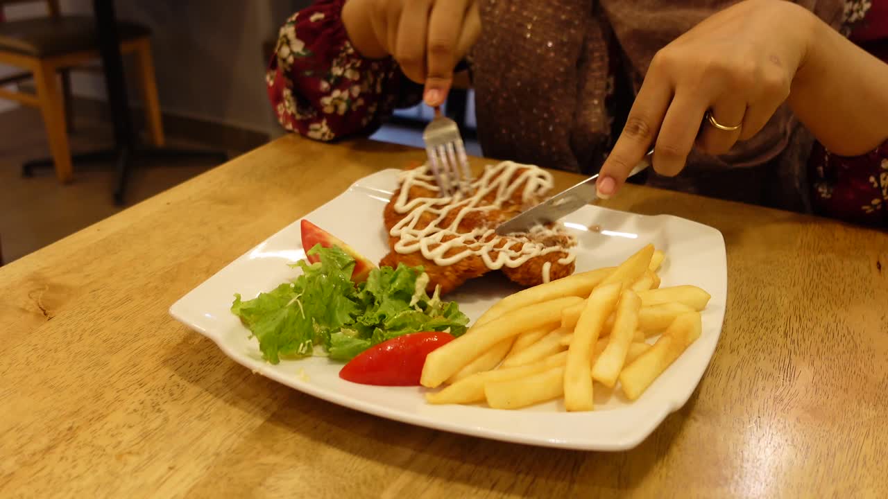 mujer comiendo una comida con chuleta, papas fritas y ensalada