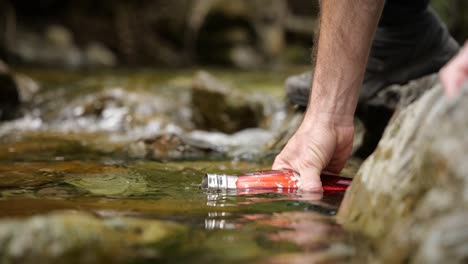 Hand-fills-up-red-thermos-bottle-with-fresh-water-in-natural-landscape