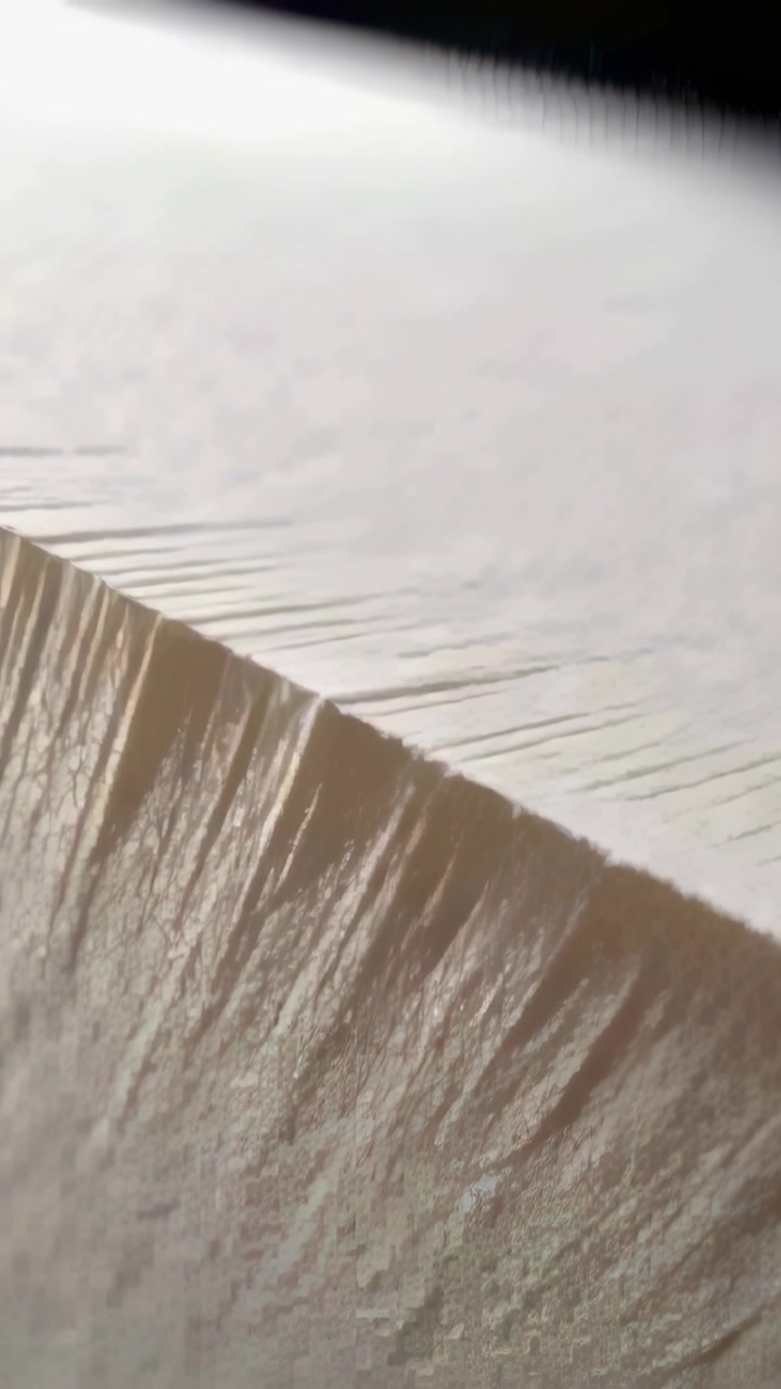 Vertical video: Panning camera showing rough cut edge of paper stack at desk, revealing texture
