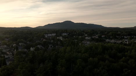 Reveladora-Foto-De-Los-Edificios-Del-Hotel-Detrás-De-Frondosos-árboles-En-La-Playa-Frente-Al-Lago-Memphremagog-En-Quebec,-Canadá-Al-Amanecer---Ascenso-De-Drones-Aéreos