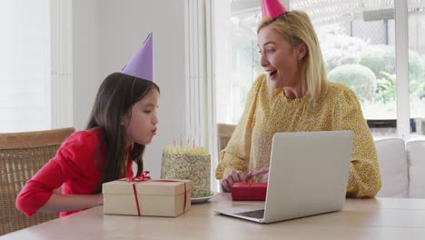 girl blowing cake while having a video chat on laptop at home