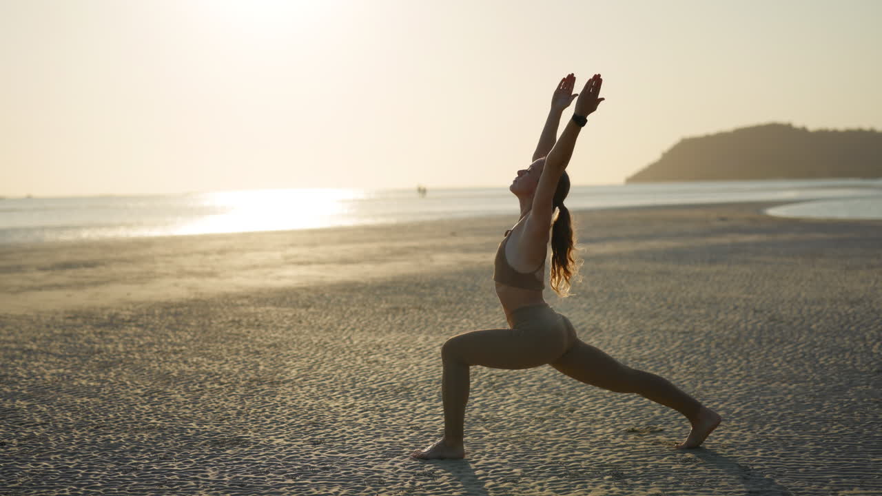 Donna che pratica la posizione del Guerriero yoga su una spiaggia all'alba