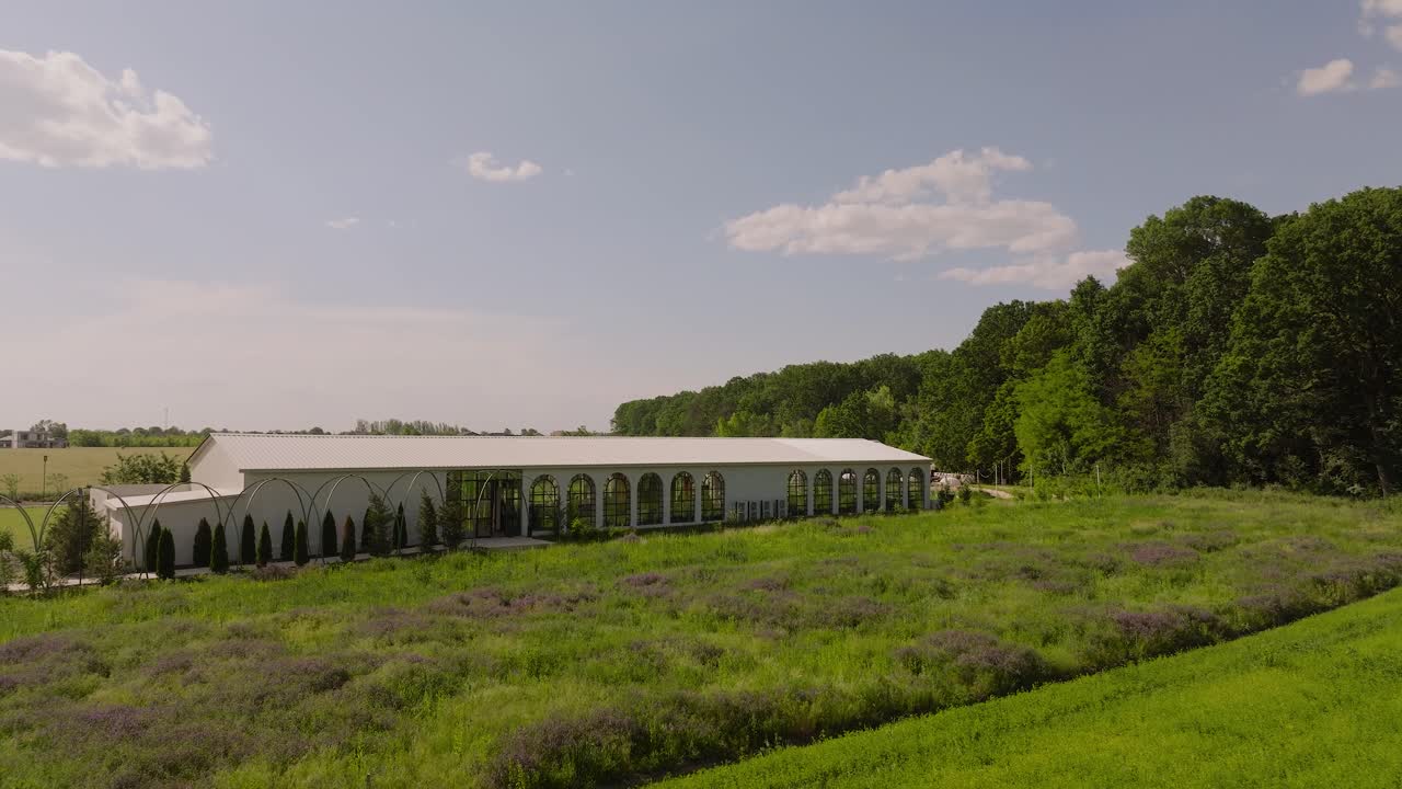 White restaurant at the edge of a green forest, surrounded by green fields on a sunny day, aerial view