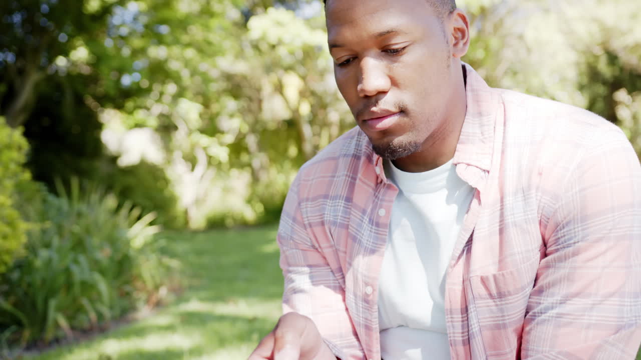 Happy african american man using smartphone in garden at home, slow motion