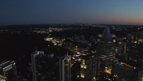 Aerial-drone-shot-slowly-flying-by-a-skyscraper-in-Buckhead,-Atlanta,-Georgia-to-reveal-the-city-lights-during-blue-hour-at-sunset-with-a-crystal-clear-sky