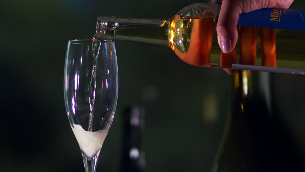 un vertido lento de vino espumoso blanco de una botella con fondo oscuro