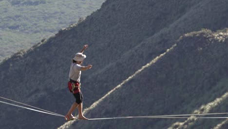 Man-balancing-and-walking-a-highline-on-the-mountains-with-forest-below-in-the-Comechingones-mountains,-San-Luis,-Argentina