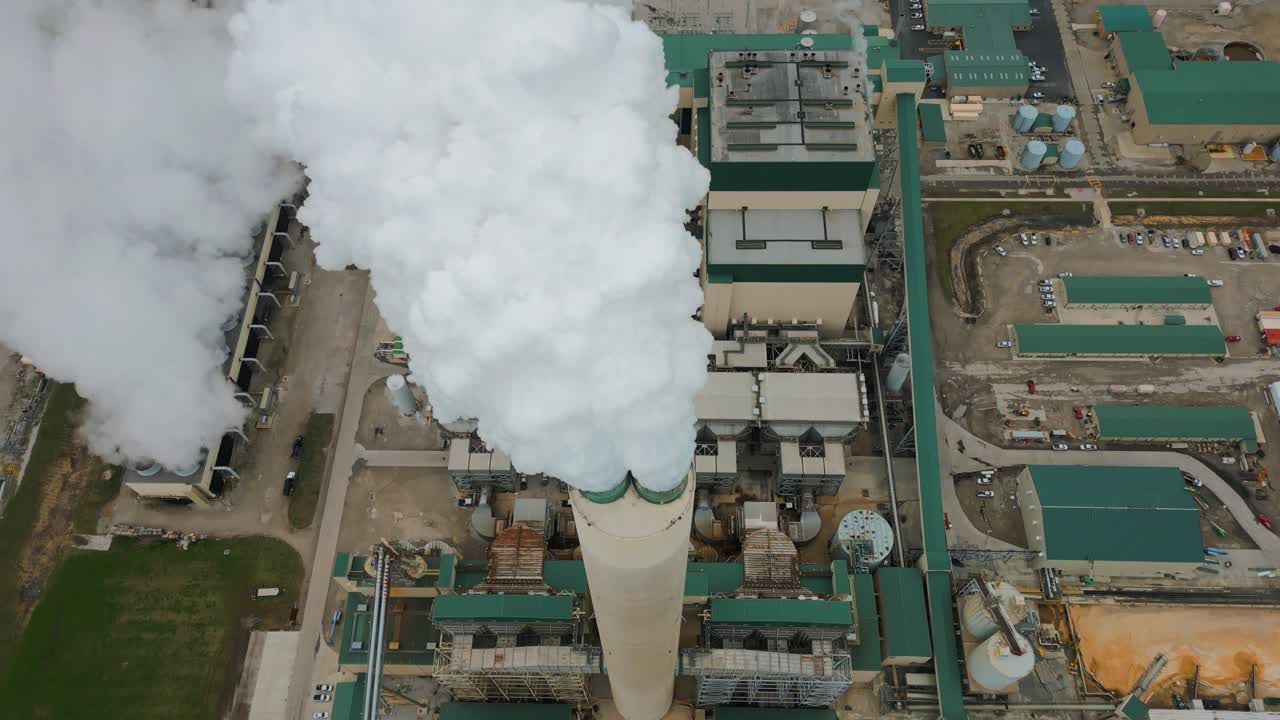 A shot looking down on a large Illinois power plant. The large smoke stack can be seen billowing out white steam as the camera flies overhead.