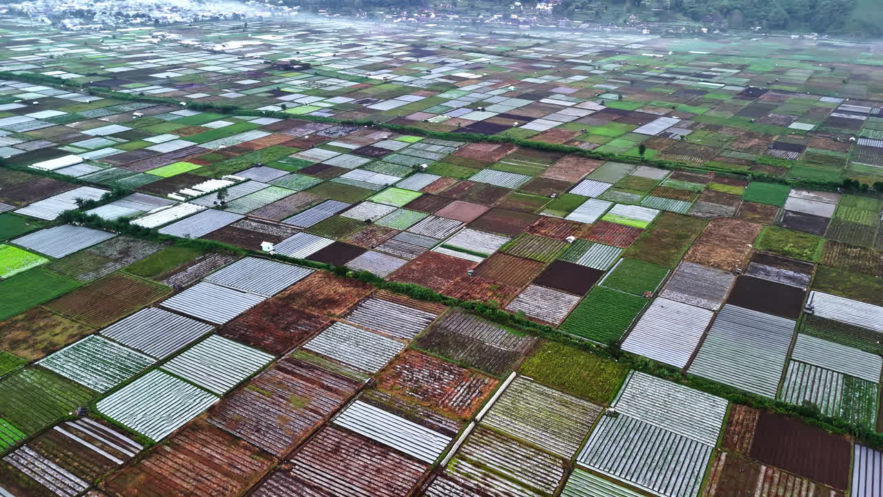 An expansive aerial view from Bukit Selong, flying over stunning patchwork of diverse agricultural fields extending towards distant mountains