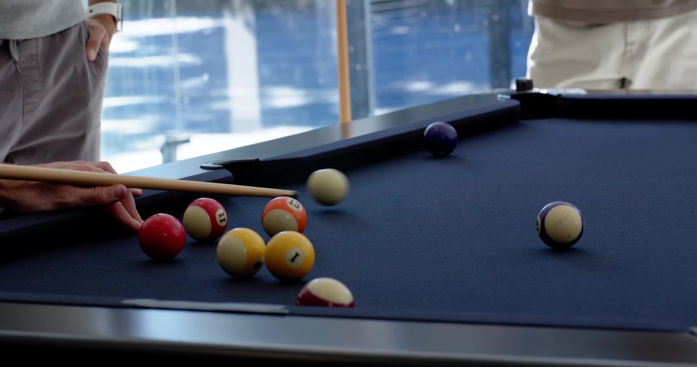 Hommes divers regardant un joueur s'aligner et frapper la bille avec la queue sur une table de billard, faisant rouler les billes pour les empocher.