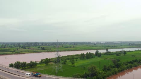 Vista-Aérea-Del-Paso-Elevado-Sobre-Tierras-Agrícolas-Cerca-Del-Río,-Y-El-Canal-Después-De-La-Lluvia-Con-Agua-Turbia-Lluviosa-Fuera-De-La-Ciudad-En-La-Región-De-Punjab,-India